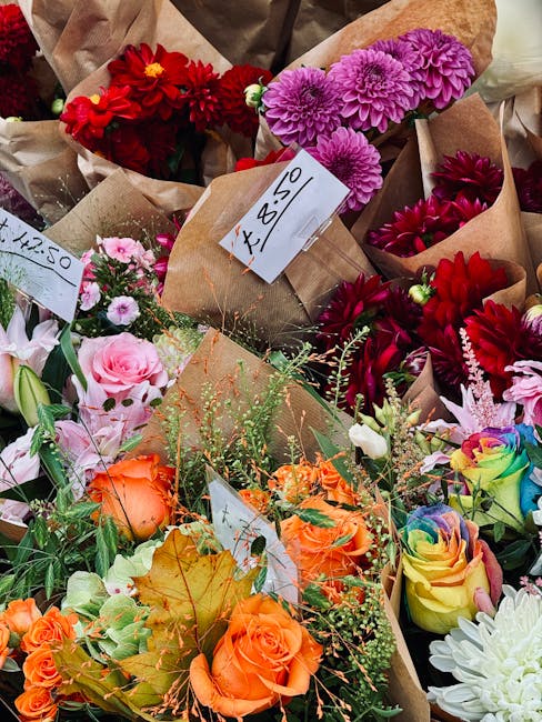 A vibrant display of fresh floral arrangements at a flower market, featuring a variety of flowers including bright red dahlias, soft pink roses, purple chrysanthemums, and multicolored roses with rain